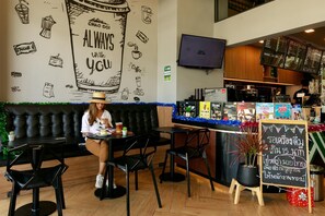 A café with a black leather couch, black chairs, a small table with a drink, and a chalkboard menu. - La Pino Hotel (Songkhla)