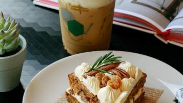 A slice of carrot cake with cream and nuts on a plate, a cup of iced coffee with whipped cream, and a small succulent plant on a table.