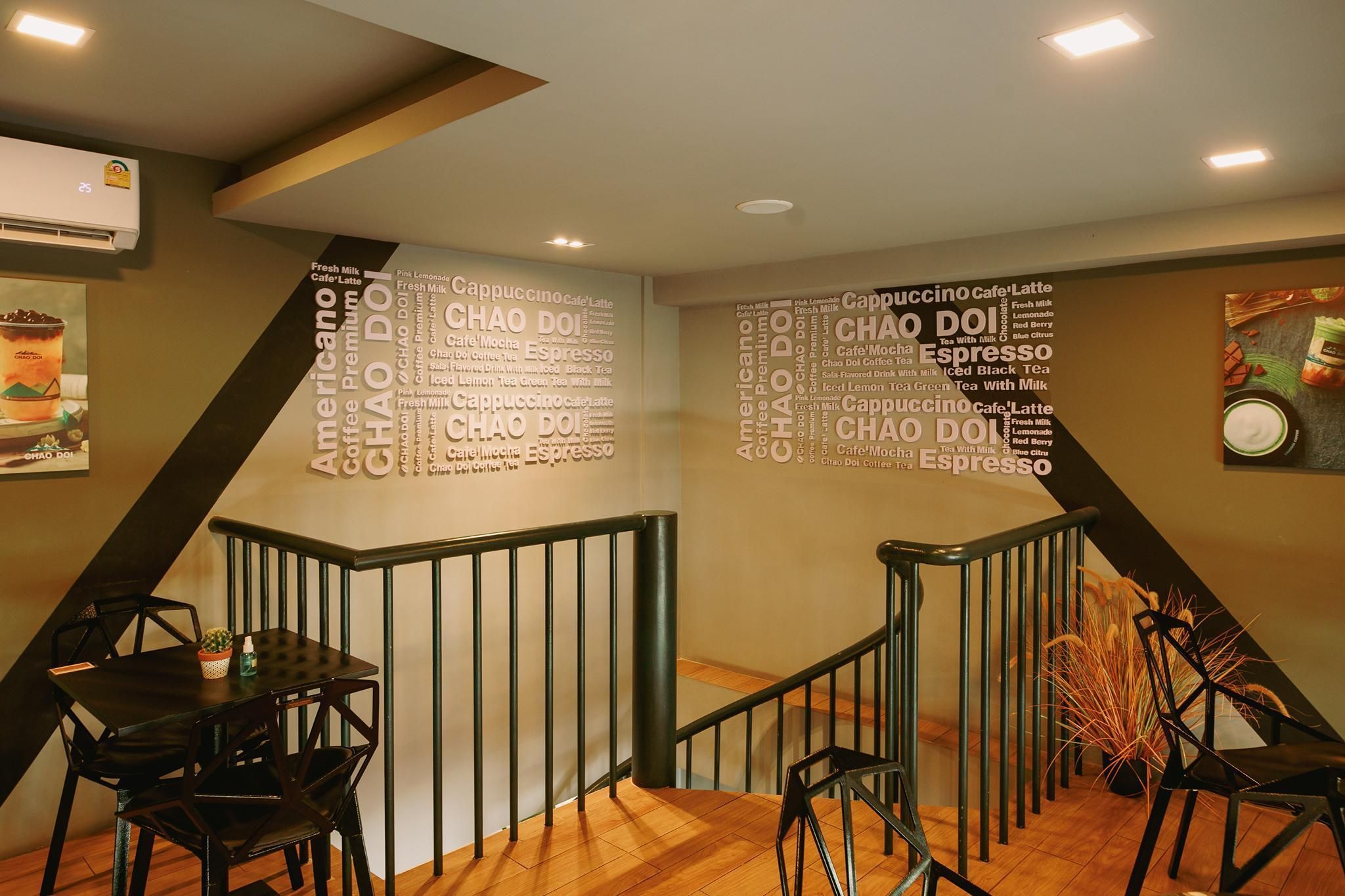 A modern interior with a staircase, a wall with a coffee-themed word cloud, and a dining area with black chairs and a table.