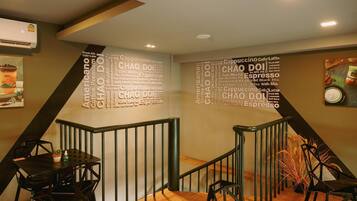 A modern interior with a staircase, a wall with a coffee-themed word cloud, and a dining area with black chairs and a table.