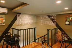 A modern interior with a staircase, a wall with a coffee-themed word cloud, and a dining area with black chairs and a table. - La Pino Hotel (Songkhla)