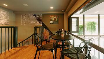 A modern cafe interior with wooden flooring, black metal chairs, and a wall with coffee-related words.
