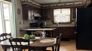 Una cocina con armarios de madera, un refrigerador negro, una mesa de comedor con sillas y un ventilador de techo.
