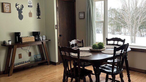 Un comedor con una mesa de madera, cuatro sillas, un ventilador de techo y una ventana con vistas a árboles.