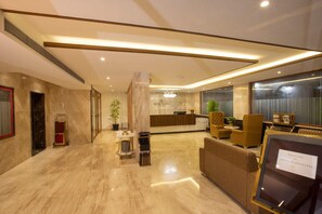A hotel lobby with a reception desk, seating area, and a sign welcoming guests to Royal Plaza Suites. - Royal Plaza Suites (Mangaluru)