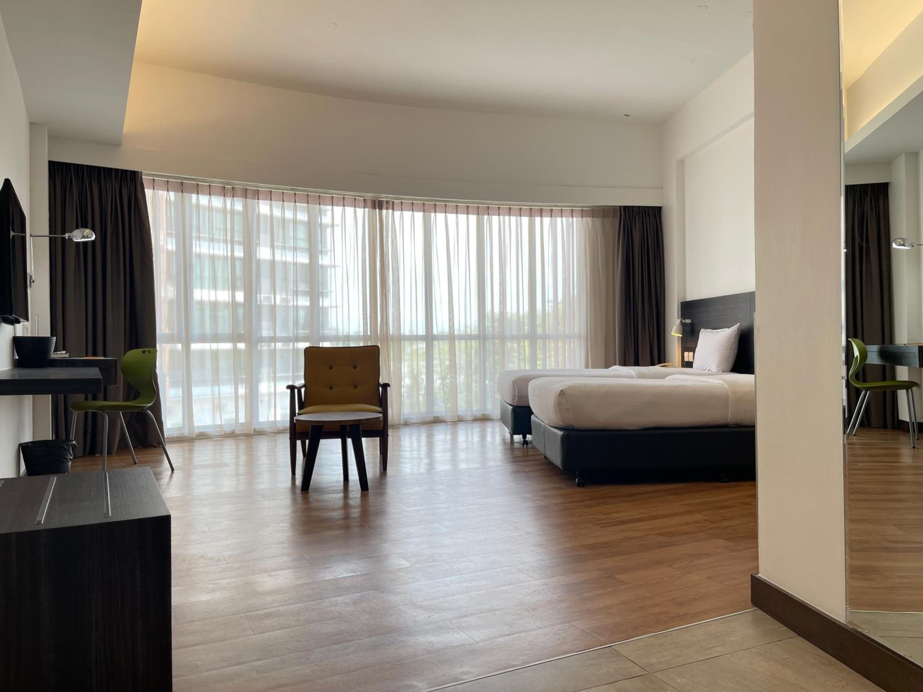 A hotel room with a bed, a desk, a chair, and large windows.