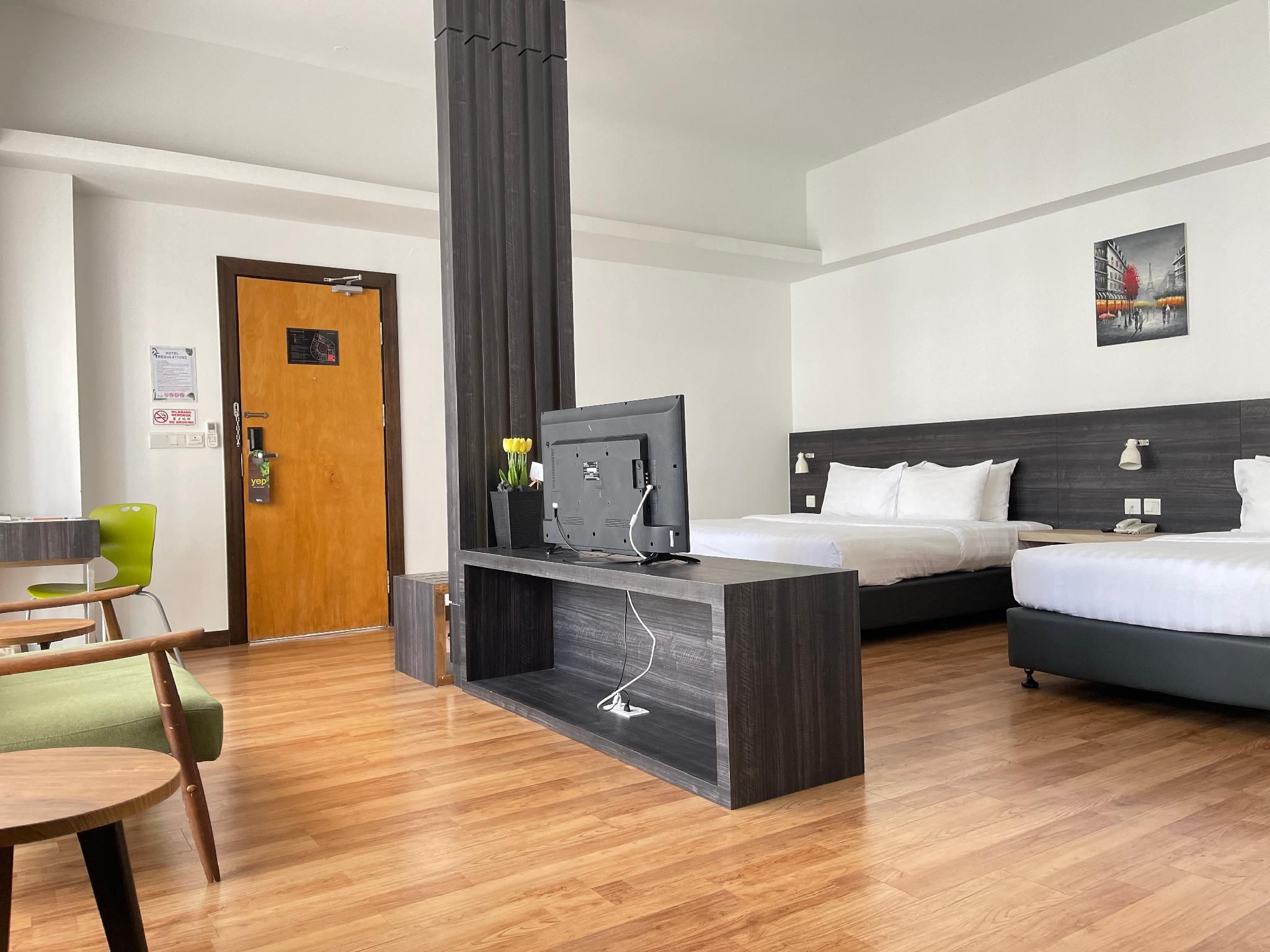 A hotel room with a bed, a desk with a television, a chair, and a door.
