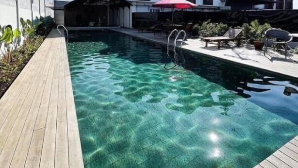 A swimming pool with clear water, a wooden deck, and a building with a modern design in the background. - Ra Inn Kemang (Jakarta)