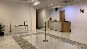 A hotel lobby with a reception desk, a small table with a vase and a potted plant, and a patterned floor. - Ra Inn Kemang (Jakarta)