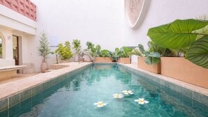Een binnenzwembad met helder water, omringd door potplanten en een betegelde vloer.