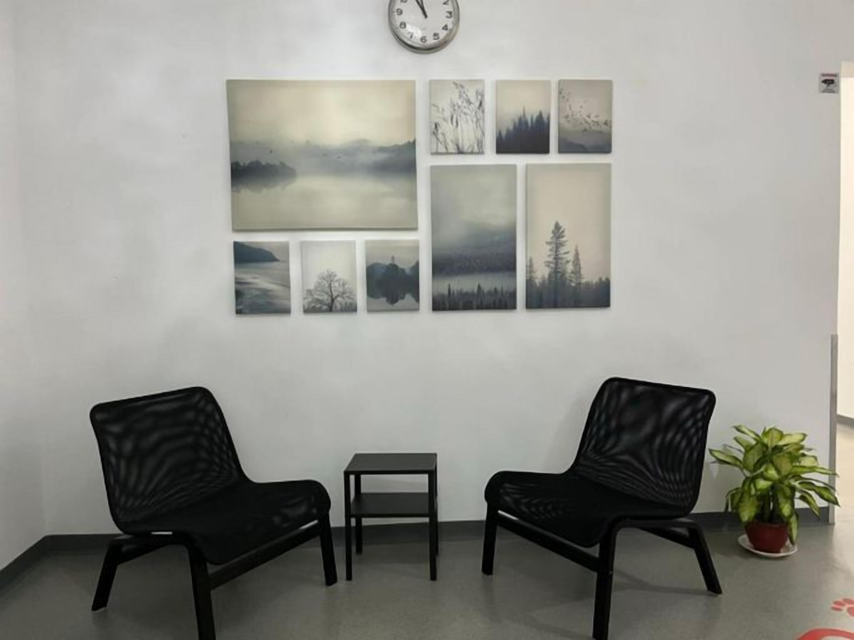 A waiting area with two black chairs, a small table, and a clock on the wall.