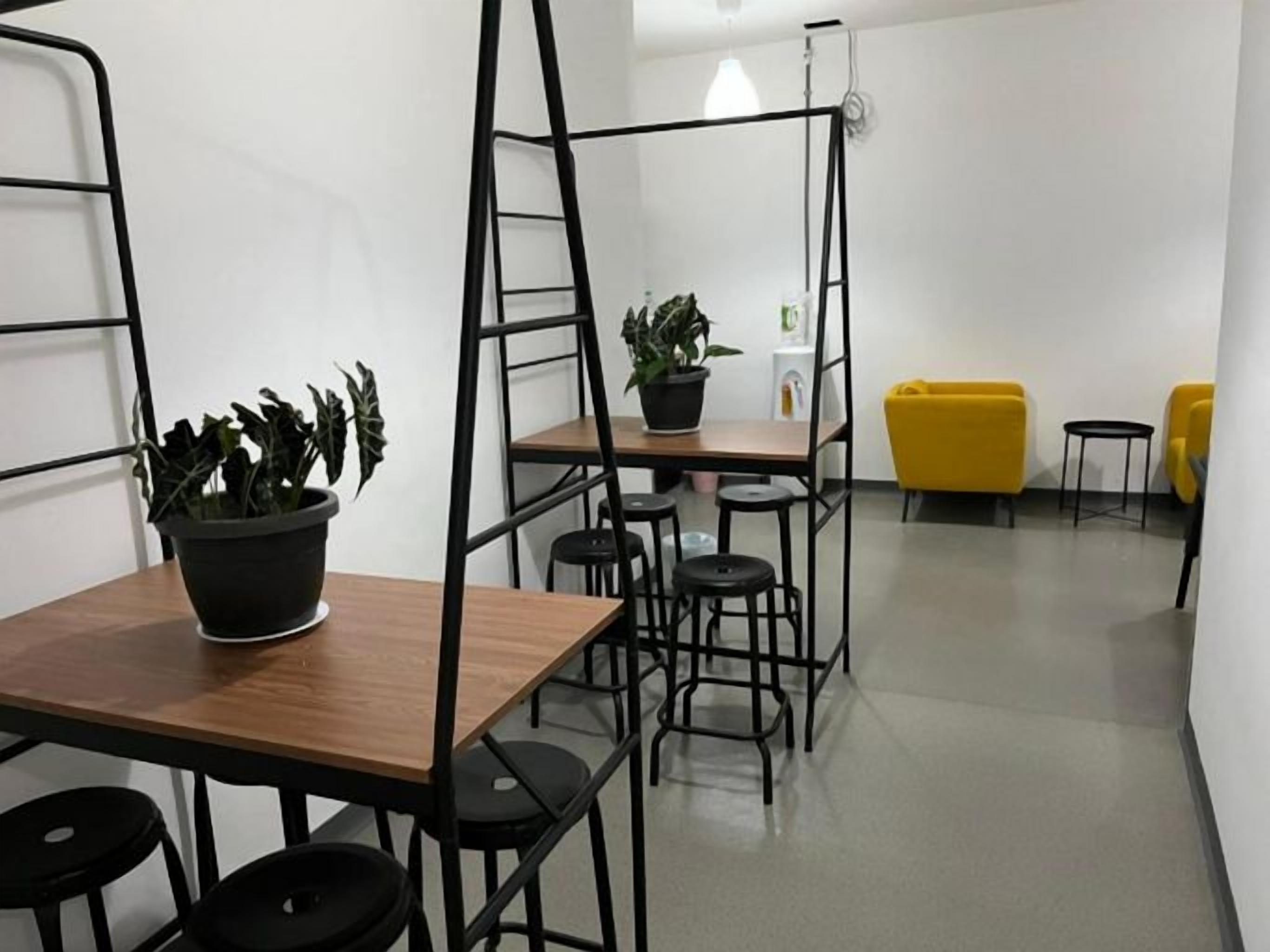 A room with a wooden table, black stools, a potted plant, a yellow couch, and a ladder.