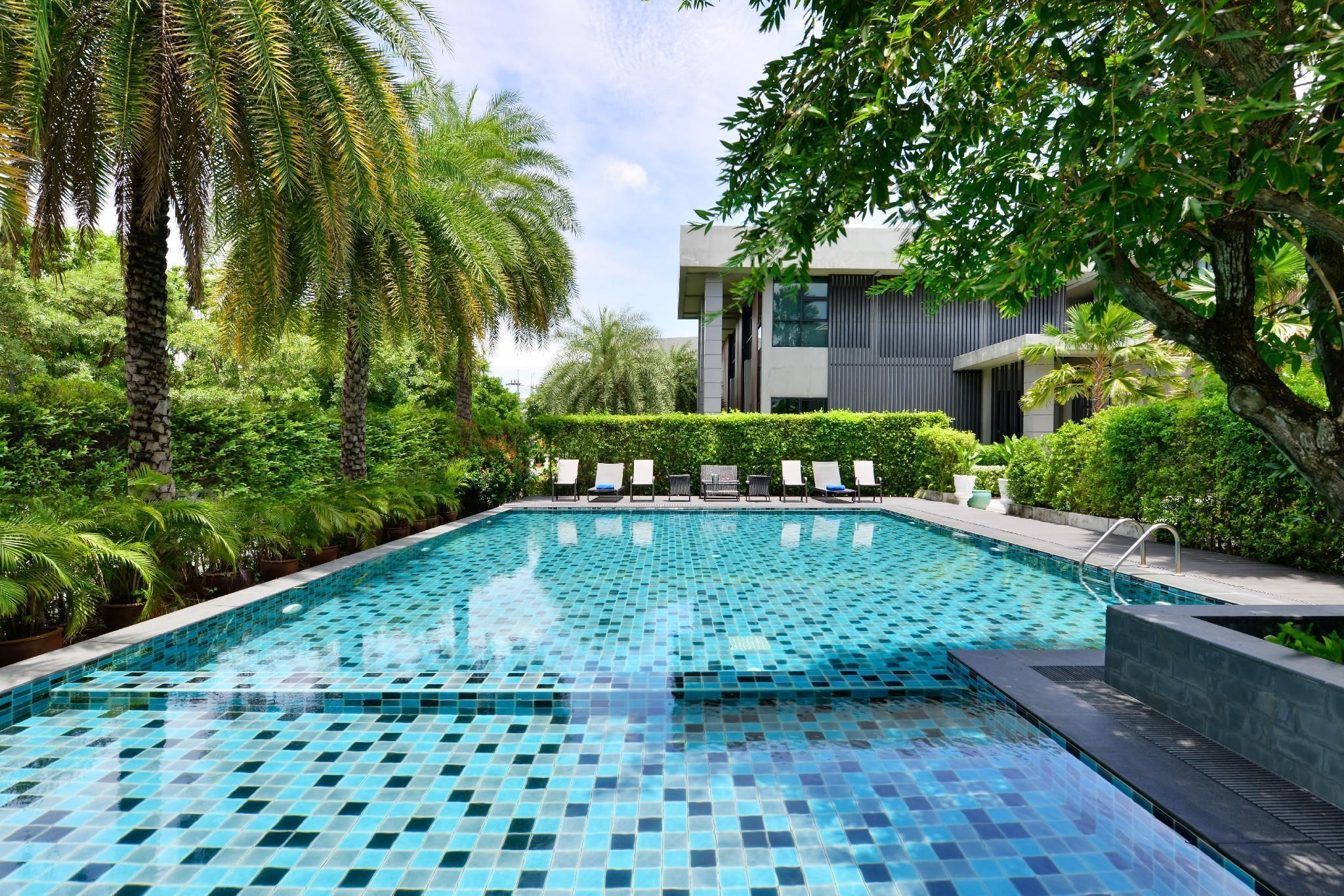 A swimming pool with tiled flooring, surrounded by lush greenery and palm trees.