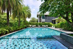 A swimming pool with tiled flooring, surrounded by lush greenery and palm trees. - Raweewan Residence (Bangkok)