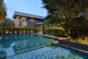 A modern building with a swimming pool, surrounded by greenery and lounge chairs. - Raweewan Residence (Bangkok)