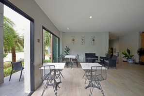 A modern indoor space with a dining area featuring metal chairs and white tables, a seating area with sofas, and a large potted plant. - Raweewan Residence (Bangkok)