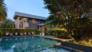 A modern building with a swimming pool, surrounded by greenery and lounge chairs. - Raweewan Residence (Bangkok)