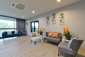 A modern living room with a sofa, chairs, and a coffee table. There are potted plants and artwork on the walls. - Raweewan Residence (Bangkok)