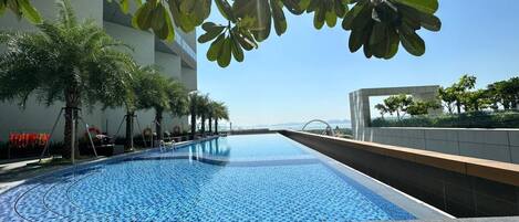 A swimming pool with a tiled edge, surrounded by palm trees and a building.