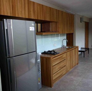 A modern kitchen with wooden cabinets, a stainless steel refrigerator, a gas stove, and a sink. - M Pavilion Karawaci (Curug)