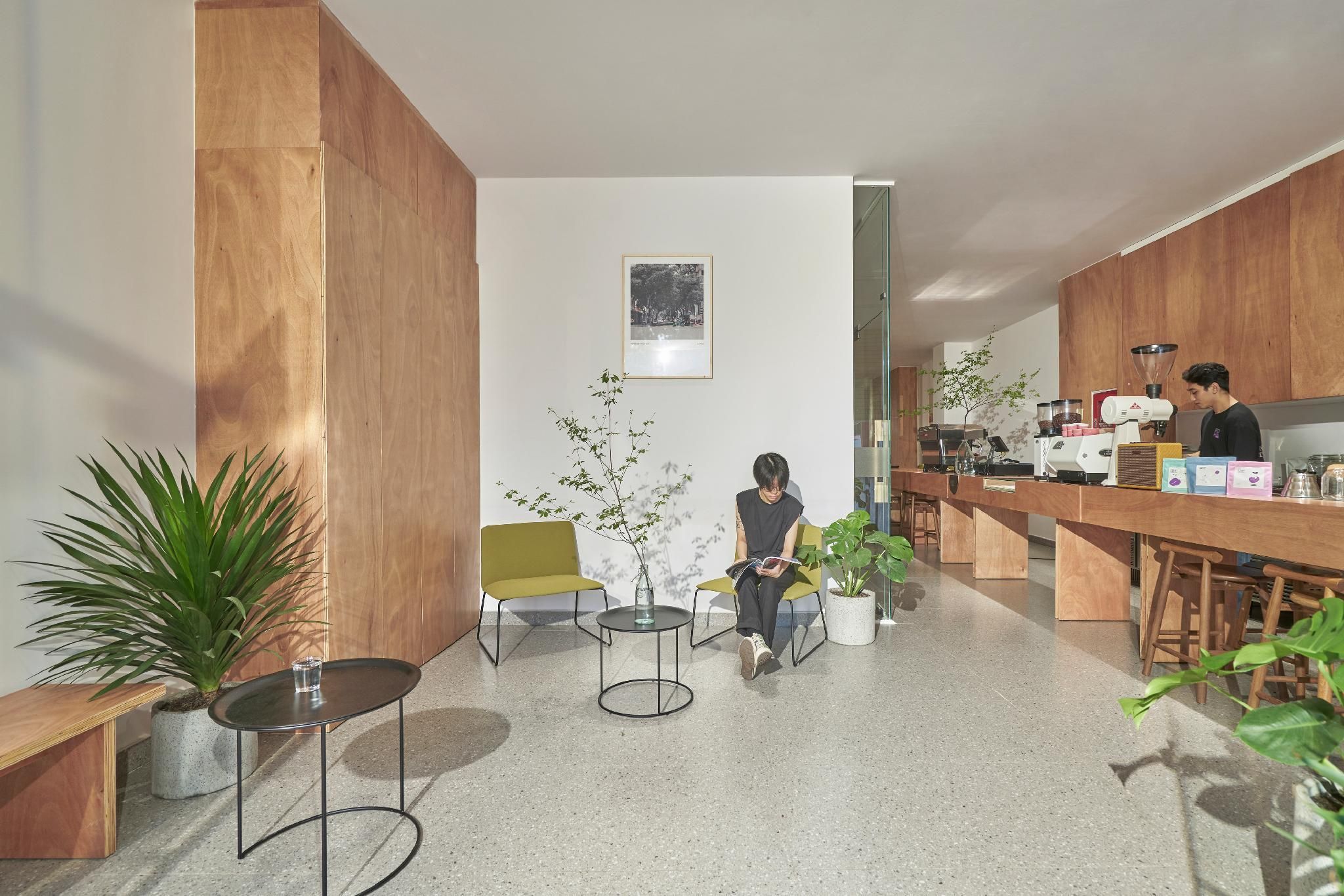 Un área de recepción moderna con paneles de madera, mostrador de recepción, asientos y plantas en macetas.