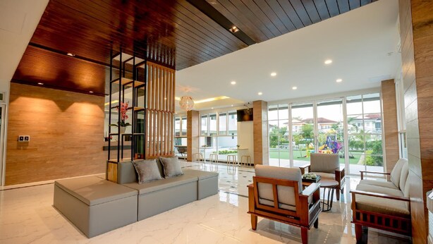 A spacious living area with a modern design, featuring a sectional sofa, wooden furniture, and large windows offering a view of the outdoors. - Gracetown Hotel Hua Hin (Hua Hin)