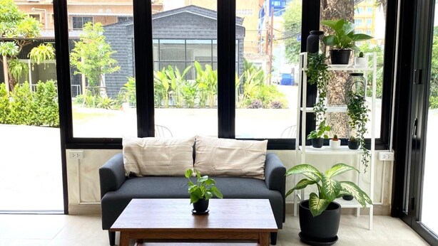 A modern living room with a grey sofa, a wooden coffee table, and a view of a cityscape through large windows. - The Shade Residence (Pattaya)
