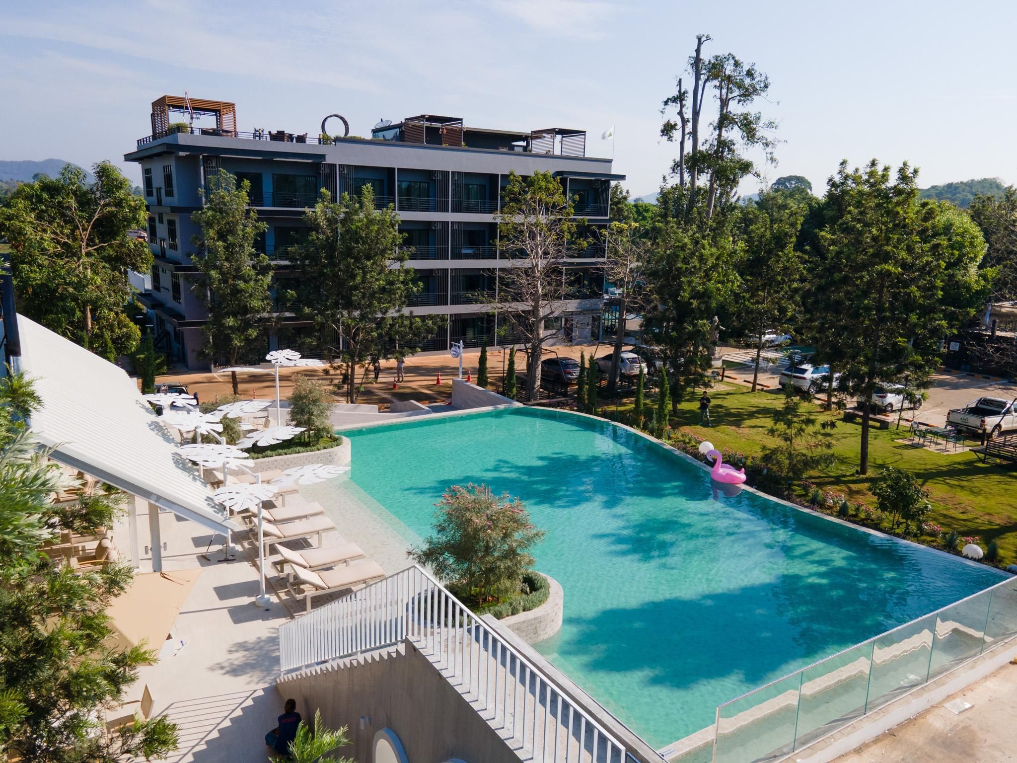 A modern hotel with a rooftop pool, surrounded by lush greenery and a clear view of the mountains.
