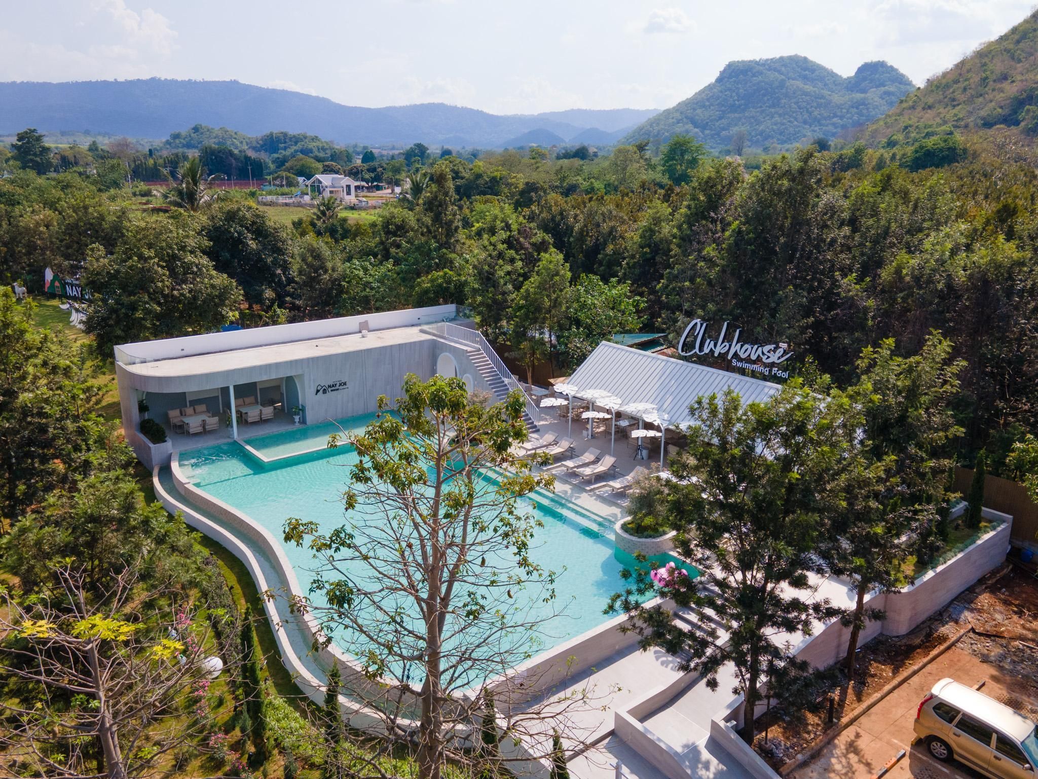 A modern hotel with a swimming pool, surrounded by lush greenery and mountains.