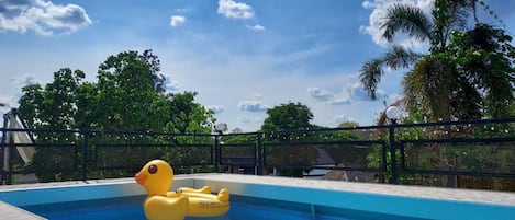 Piscina com um pato inflável amarelo, cercada por uma grade e árvores.