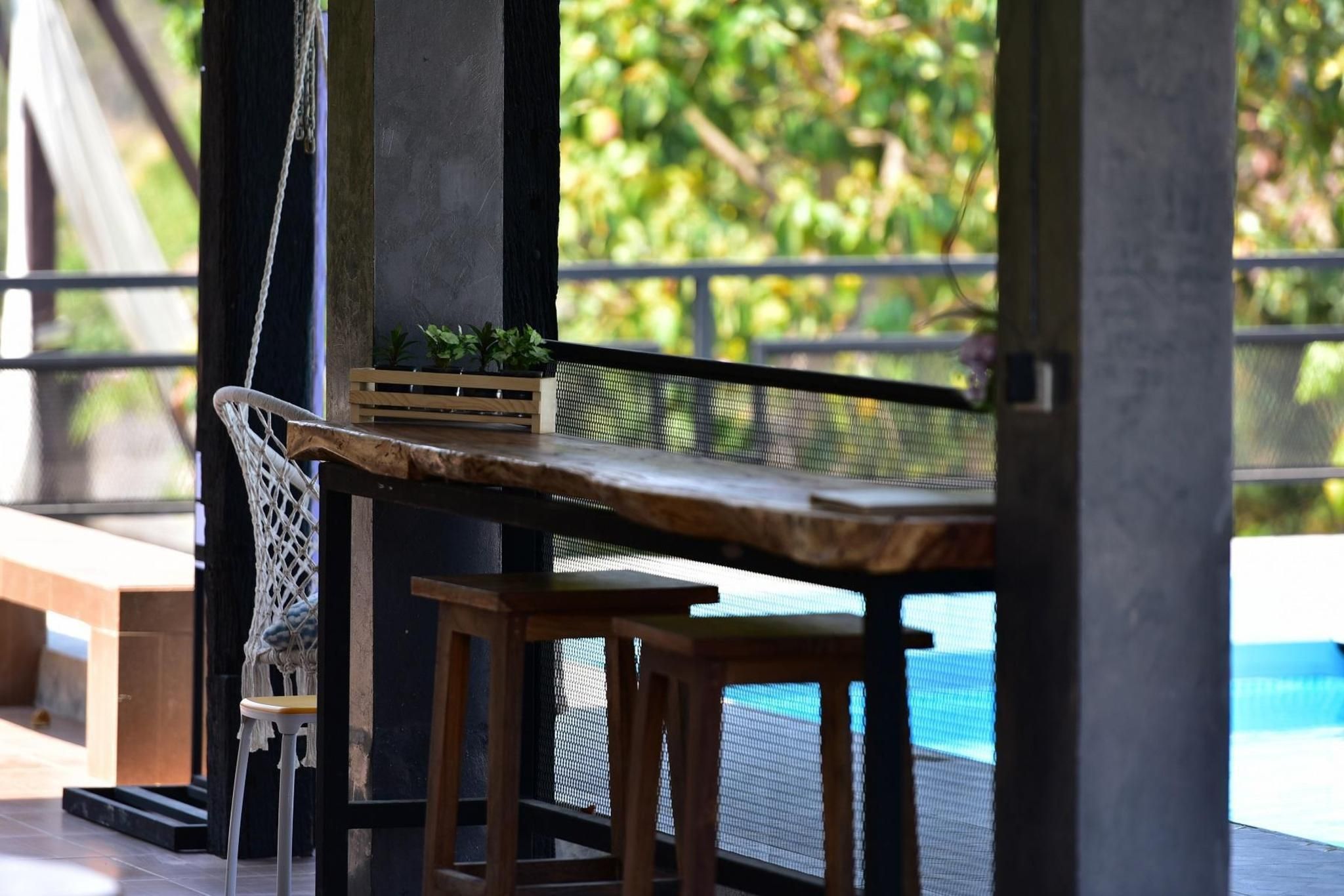 A wooden table with a plant, a woven chair, and a view of a swimming pool.