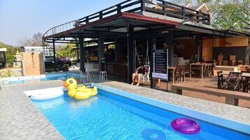 A swimming pool with inflatable toys, a covered seating area, and a bar.