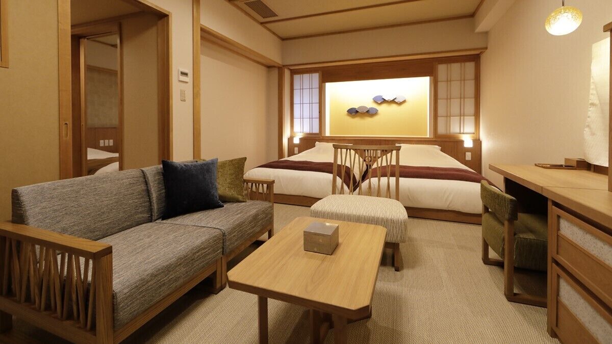 A traditional Japanese-style room with a sofa, a small table, a bed with a wooden headboard, and a wall-mounted shelf.