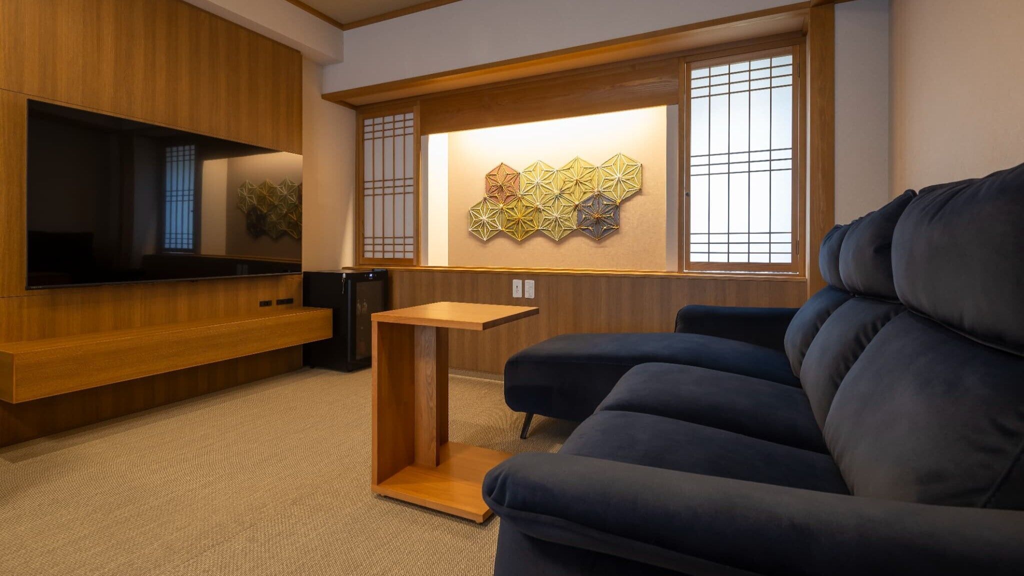 A modern living room with a flat-screen TV, a dark sofa, a small wooden table, and decorative wall art.