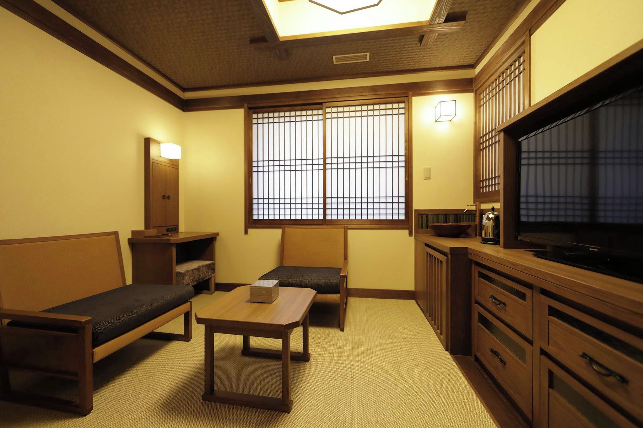 Una habitación tradicional japonesa con suelo de tatami, una mesa baja, un sofá, un armario y un televisor.