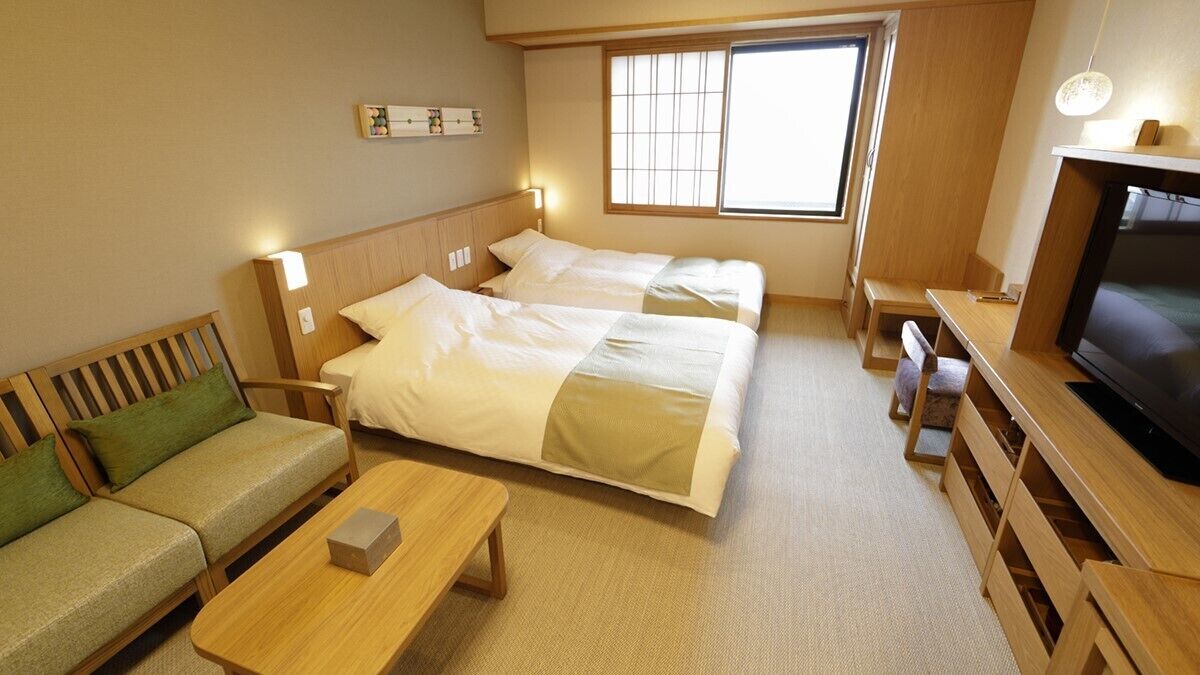 A hotel room with two beds, a sofa, a TV, and a window.