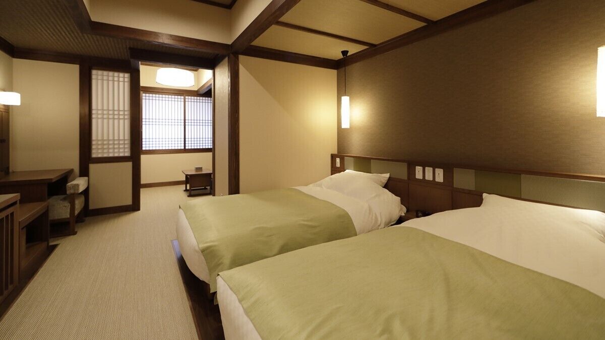 A hotel room with two beds, a desk, a chair, and a traditional sliding door.