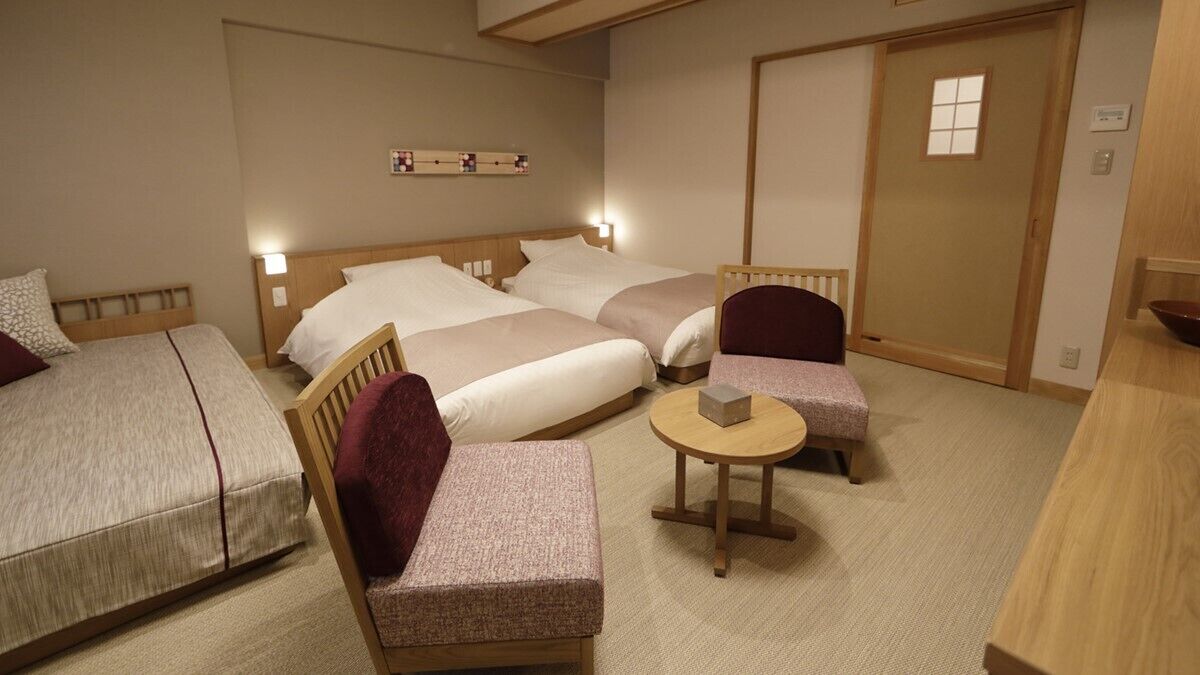 A hotel room with two beds, a small round table, a chair, and a wooden cabinet.