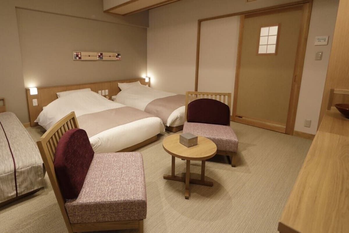 A hotel room with two beds, a small round table, a chair, and a wooden cabinet.