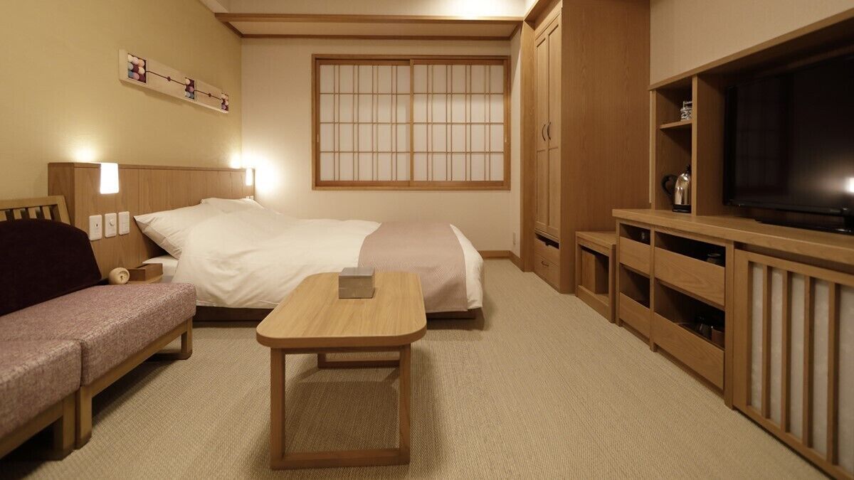 A hotel room with two beds, a sofa, a small table, a TV, and wooden cabinets.