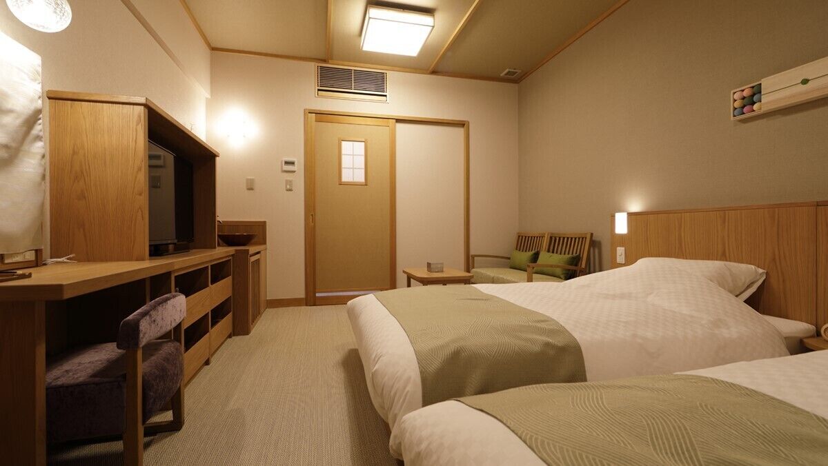 A hotel room with two beds, a desk with a chair, a television, and a small table.