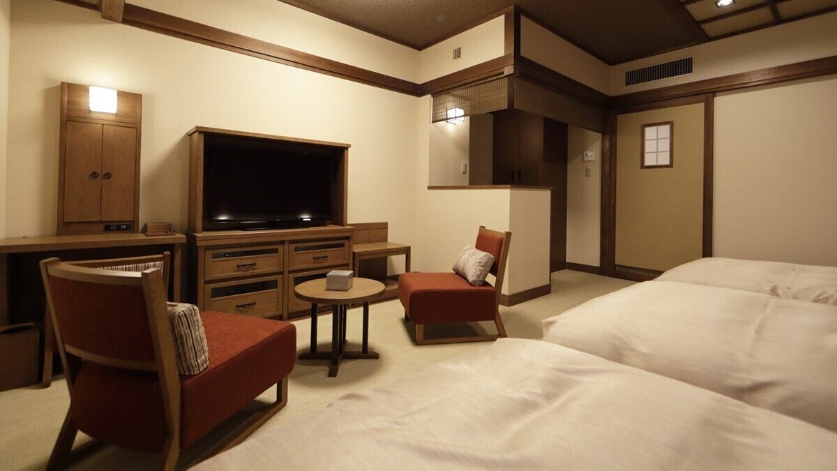A hotel room with a bed, a TV, a desk, a chair, and a small table.