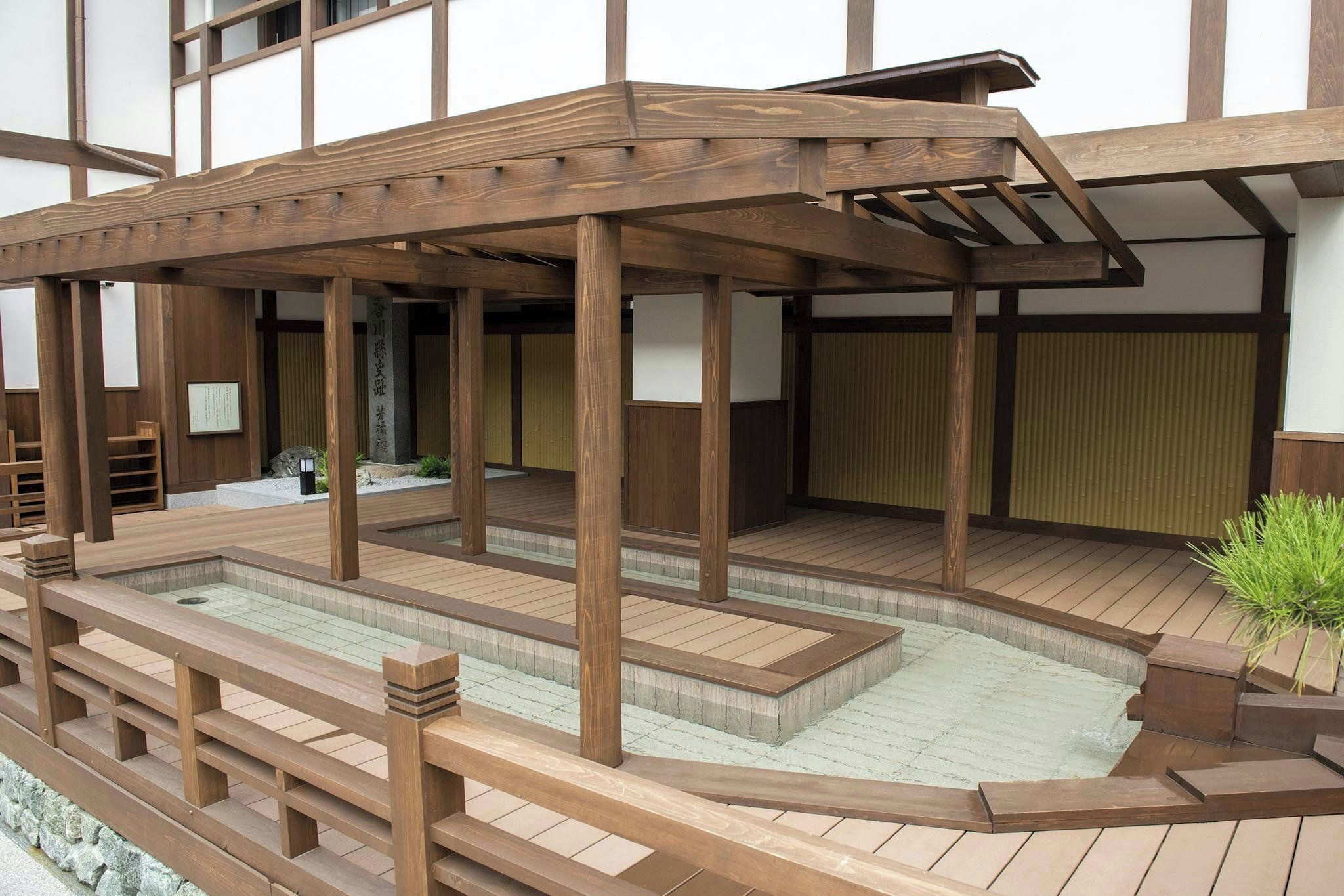Zona de aguas termales al aire libre de estilo japonés tradicional, con construcciones de madera y una balsa de piedra.