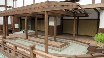 Zona de aguas termales al aire libre de estilo japonés tradicional, con construcciones de madera y una balsa de piedra.