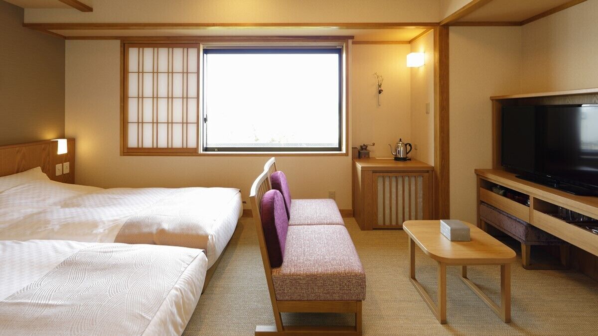 A hotel room with two beds, a television, a small table, and a window with a view.