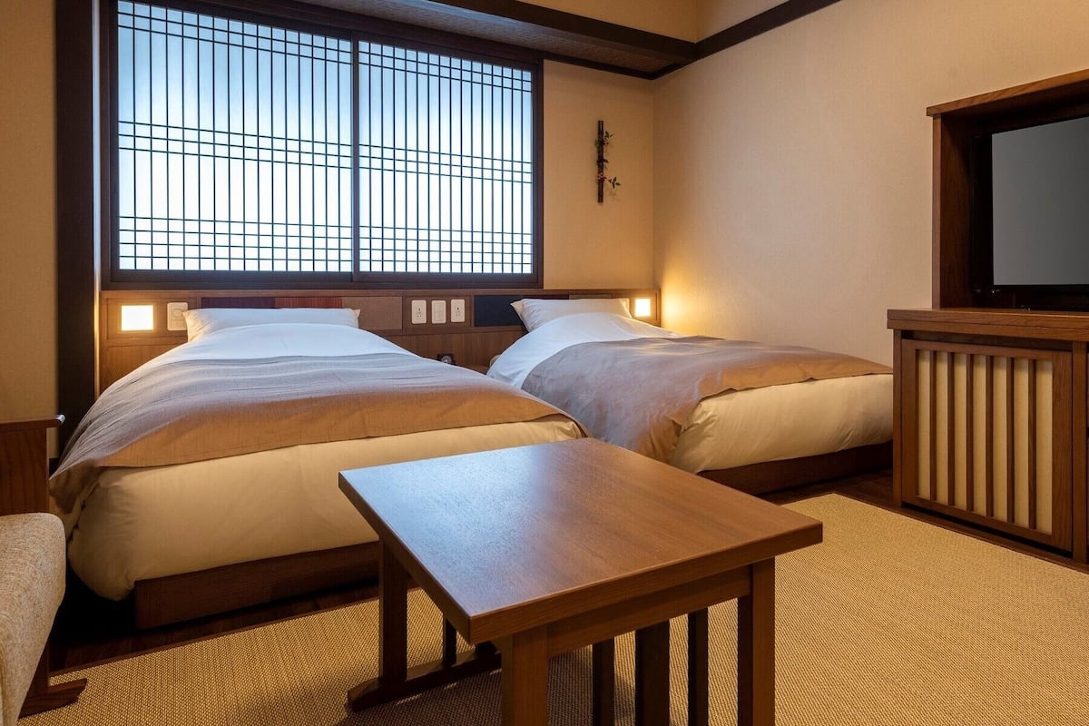 A hotel room with two beds, a television, a small table, and a window with a view.