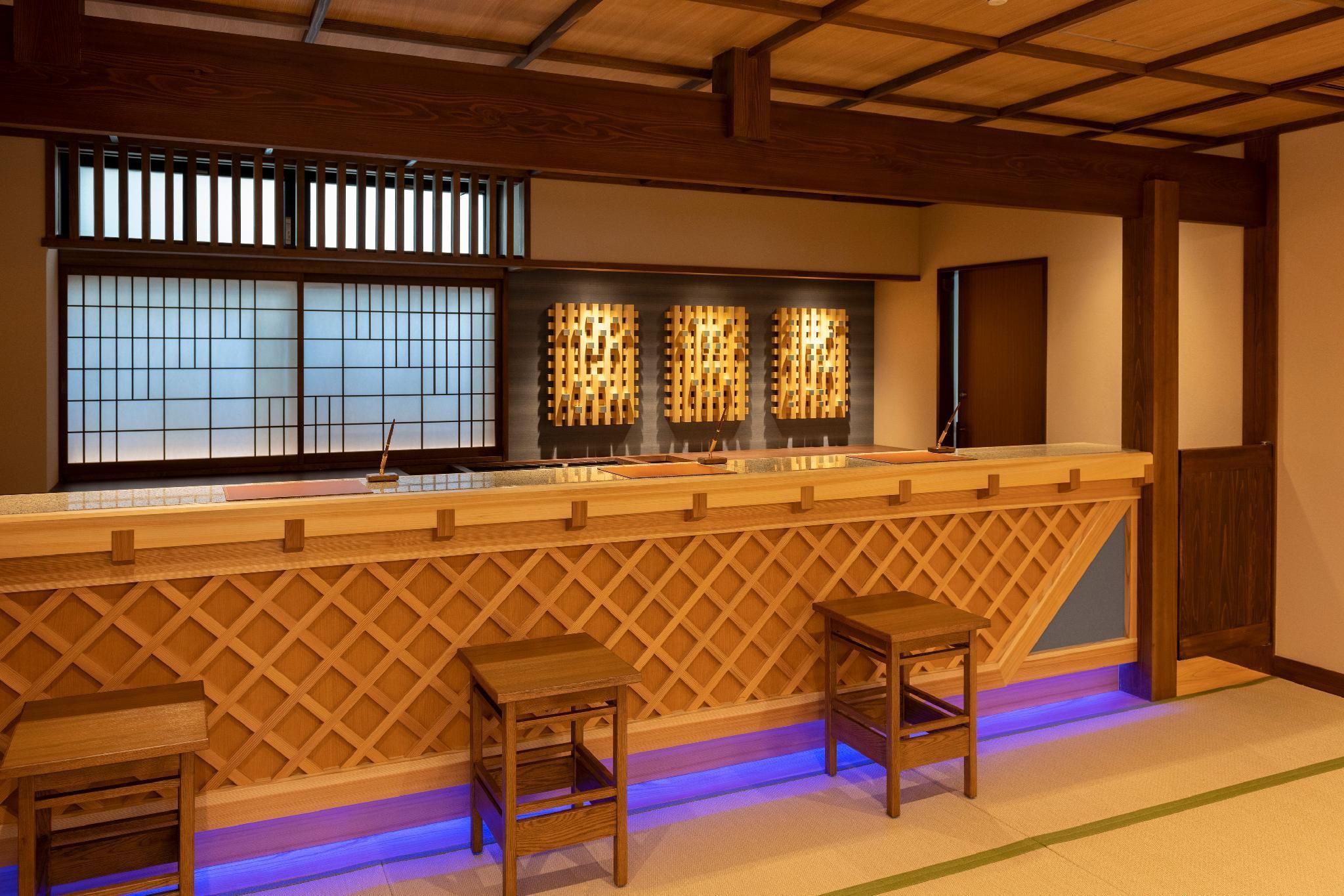 A traditional Japanese-style bar with wooden lattice partitions, a low counter, and two stools.