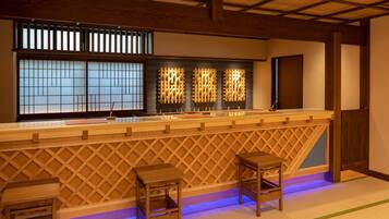 A traditional Japanese-style bar with wooden lattice partitions, a low counter, and two stools.
