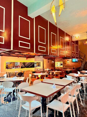 Een restaurant interieur met hoge tafels en stoelen, een trap en een televisiescherm aan de muur.