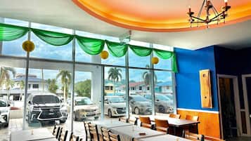 A restaurant with large windows, green drapes, and a chandelier.